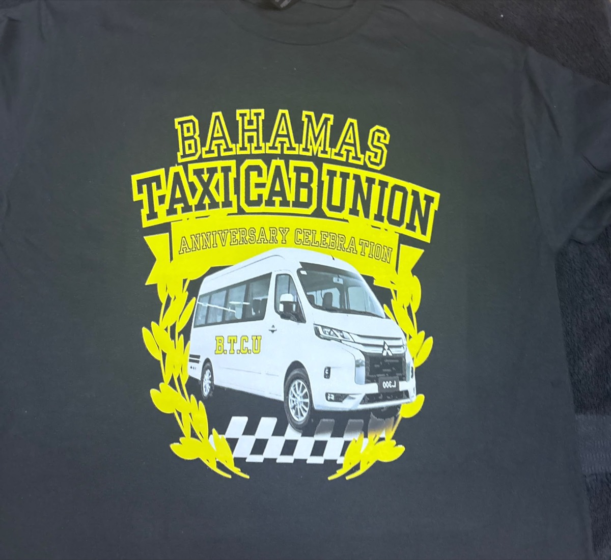 Dark tee with a yellow Bahamas Taxi Cab Union anniversary crest